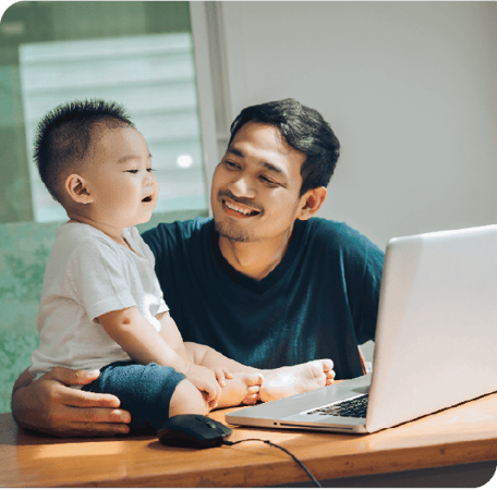 An image showing a father and his young son smiling and playing together on a laptop.