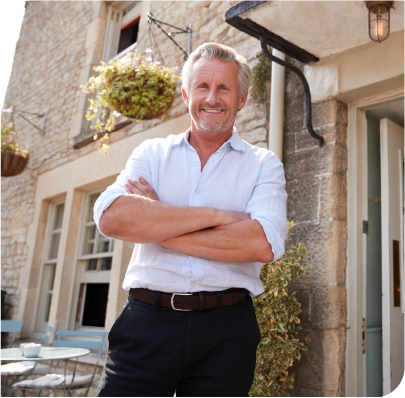 Image of smiling building owner standing in front of his property with arms crossed.