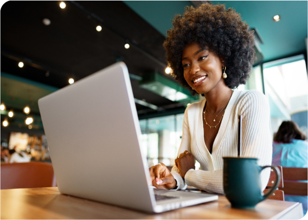 Diverse businessman smiling on laptop with coffee mug at cafe