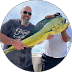 A smiling man in sunglasses and a beard holds up a large, yellow and blue mahi-mahi fish.